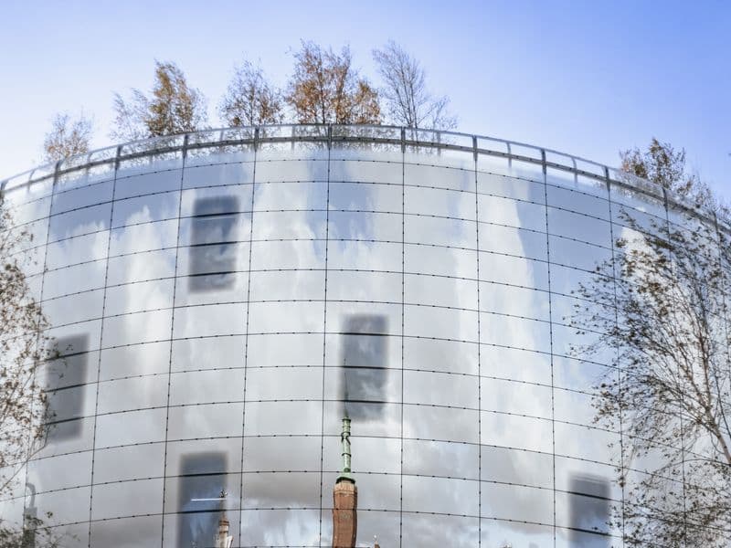 Modern building with reflective glass and sky imagery, surrounded by trees.