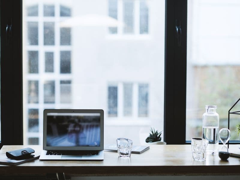Sleek office desk setup featuring a laptop, glass of water, and open window view.